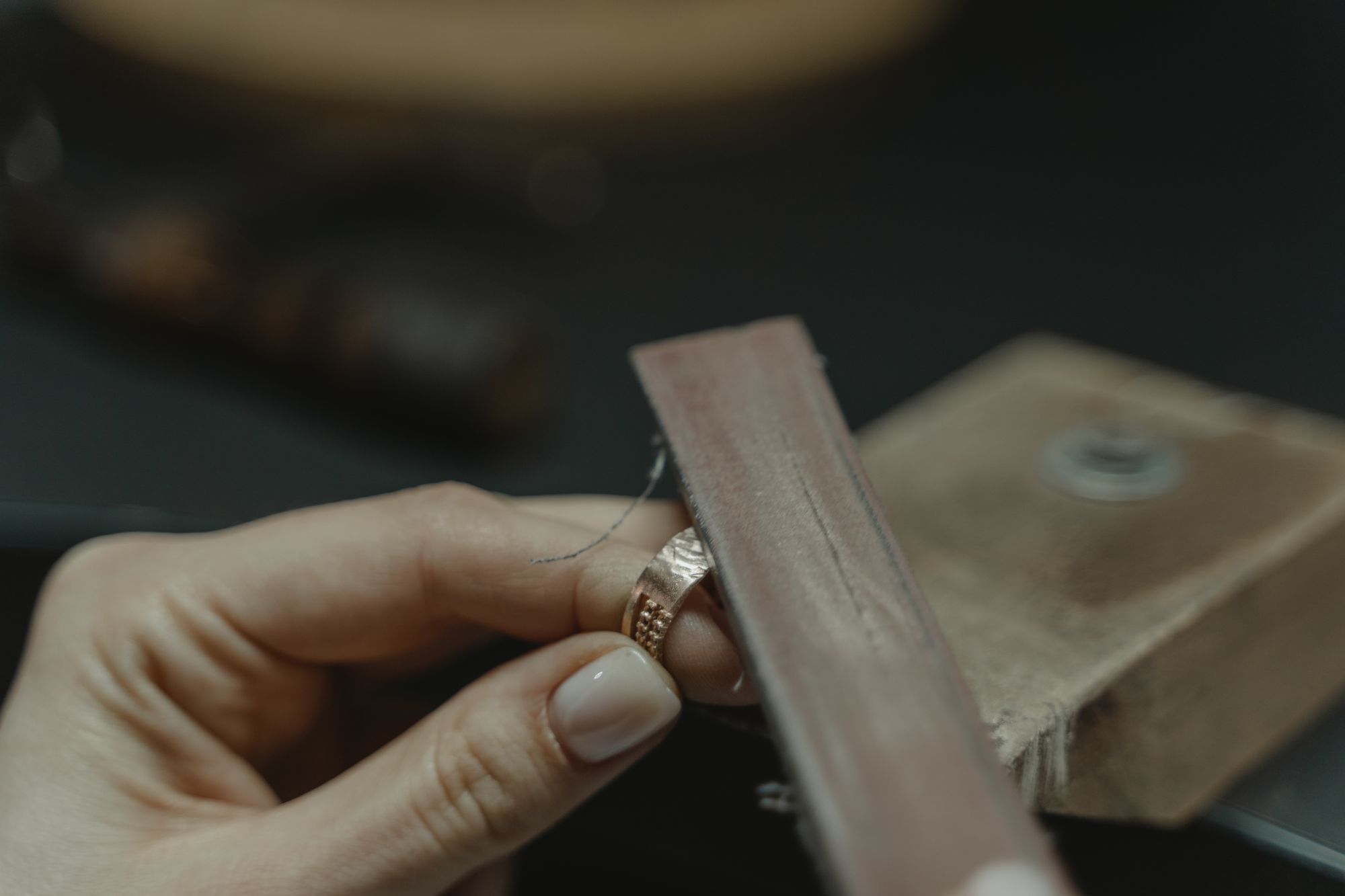 Eine Hand führt einen Goldring mit gehämmerter Oberfläche an einer Feile entlang