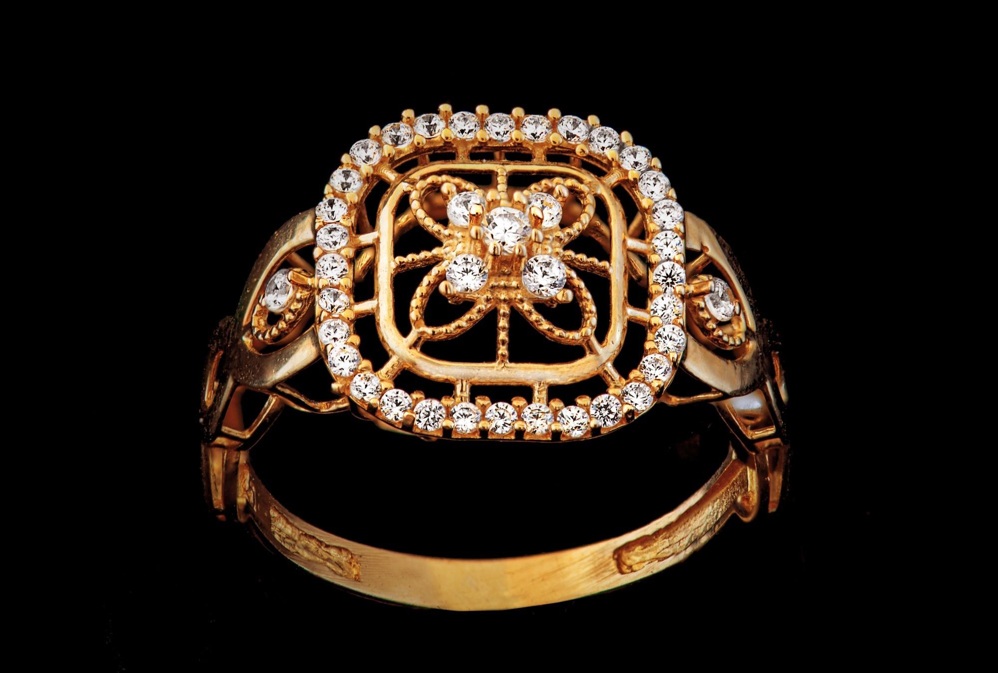 Goldener Ring mit durchbrochenem Ringkopf und kleinen weißen Steinen vor schwarzem Grund
