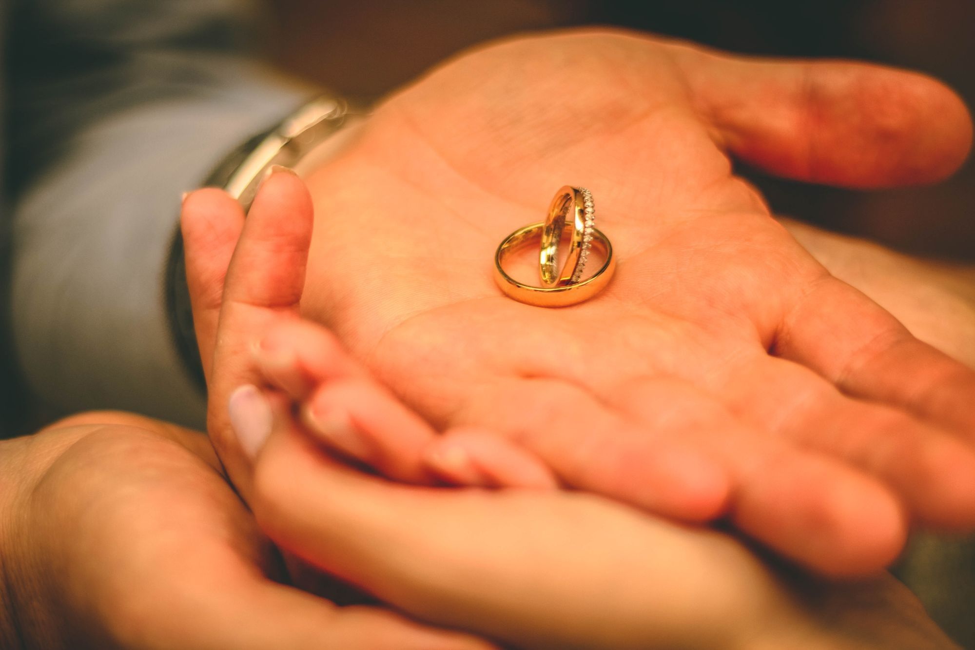 Zwei Hände liegen ineinander, in der offenen Handfläche zwei goldene Ringe