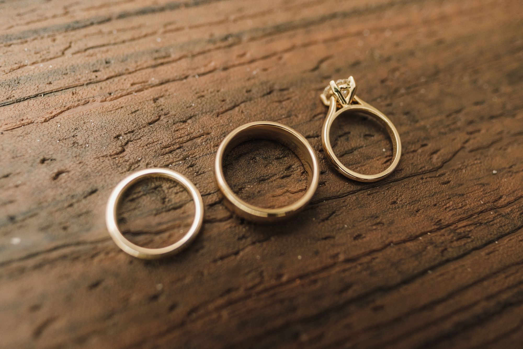 Zwei goldene Ringe und ein Ring mit Stein liegen auf einer Holzplatte