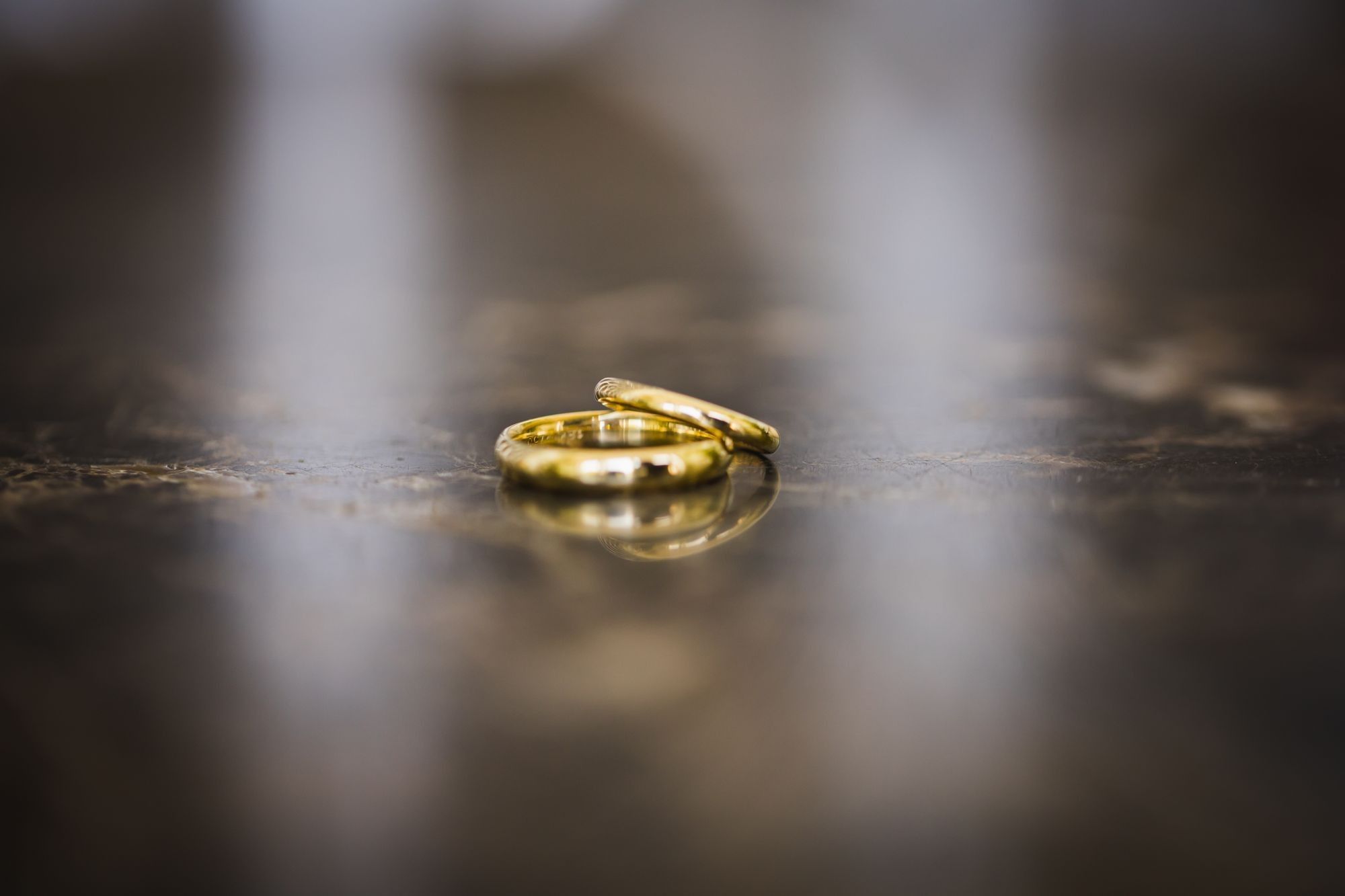 Zwei goldene Trauringe liegen aneinander auf einer dunklen, spiegelnden Steinplatte